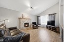 Living area featuring a stone-clad fireplace with a wood mantel, vaulted ceiling with track lighting, and wood-finish flooring - 1729 65 Street, Edmonton, AB  - Indoor Photo Showing Living Room With Fireplace 