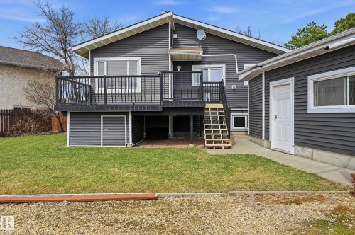 Rear exterior featuring dark gray horizontal siding, an elevated deck with black railing, a concrete patio, a ground-level storage area, and a detached garage with a white door - 1729 65 Street, Edmonton, AB - Outdoor With Deck Patio Veranda