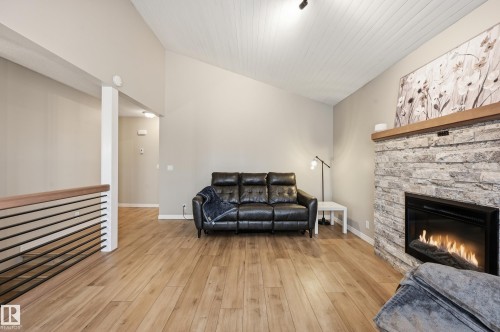 Living area featuring a floor-to-ceiling stone fireplace with a wood mantle, vaulted ceilings with wood paneling, and wood-finish flooring - 1729 65 Street, Edmonton, AB - Indoor Photo Showing Living Room With Fireplace