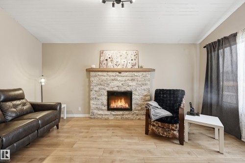 Living area featuring a stone-clad fireplace with a wood mantel, wood-finish flooring, and a white plank ceiling - 1729 65 Street, Edmonton, AB - Indoor Photo Showing Living Room With Fireplace