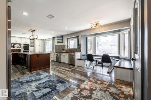 Open-concept kitchen featuring wood-finish flooring, a central island with countertop seating, stainless steel appliances, a tile backsplash, and a bay window dining area with built-in bench seating - 7 Doolan Place, St. Albert, AB - Indoor