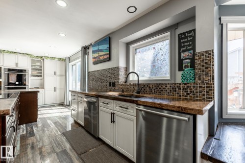 Kitchen featuring wood-finish flooring, white cabinetry, integrated double oven, and stainless steel dishwasher - 7 Doolan Place, St. Albert, AB - Indoor Photo Showing Kitchen With Upgraded Kitchen