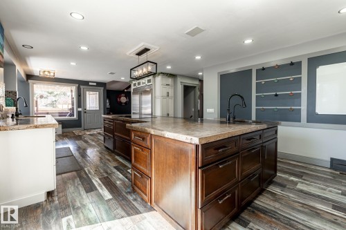 Kitchen featuring dual islands with stone countertops, dark wood cabinetry, and a modern linear chandelier - 7 Doolan Place, St. Albert, AB - Indoor Photo Showing Kitchen With Upgraded Kitchen