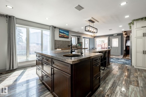 Kitchen featuring a large central island with a built-in sink and stone countertop, wood-finish flooring, recessed lighting, and white cabinetry - 7 Doolan Place, St. Albert, AB - Indoor Photo Showing Kitchen