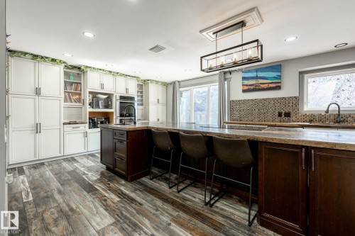 Spacious kitchen featuring an expansive island with seating, dark wood-finish cabinetry, and light-toned upper cabinetry - 7 Doolan Place, St. Albert, AB - Indoor Photo Showing Kitchen
