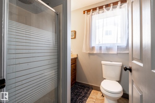 Bathroom featuring a stand-up shower with frosted glass enclosure, a window with sheer curtains, a toilet, a vanity with a countertop, and tiled flooring - 7 Doolan Place, St. Albert, AB - Indoor Photo Showing Bathroom
