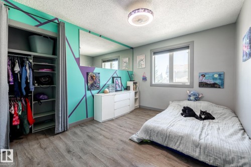 Bedroom featuring wood-finish flooring, a contemporary ceiling light fixture, a window with a roller shade, and an organized closet with shelving and hanging space - 7 Doolan Place, St. Albert, AB - Indoor Photo Showing Bedroom