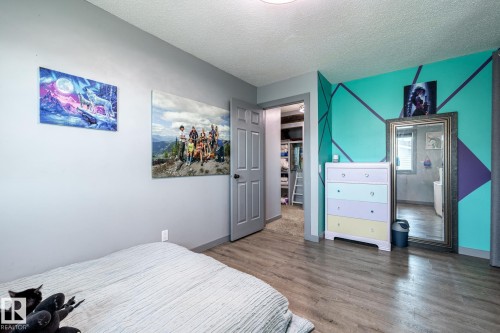 Room featuring wood-finish flooring, a neutral gray wall, and a vibrant accent wall with geometric design - 7 Doolan Place, St. Albert, AB - Indoor Photo Showing Bedroom