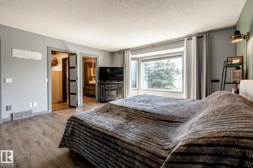 Bedroom featuring wood-finish flooring, a bay window with drapes, and a built-in media console with an integrated electric fireplace - 7 Doolan Place, St. Albert, AB - Indoor Photo Showing Bedroom
