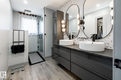 Dual vessel sinks set on a dark countertop with a sleek, grey vanity below - 7 Doolan Place, St. Albert, AB - Indoor Photo Showing Bathroom