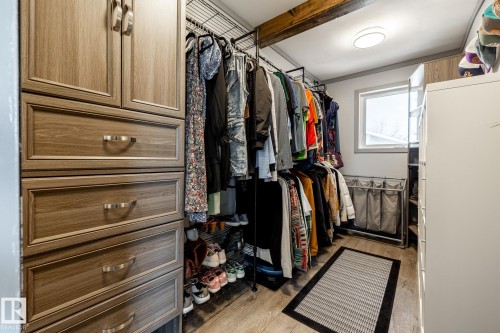 Custom closet system featuring wood-finish cabinetry with brushed nickel hardware, open shelving, and a prominent exposed wood beam - 7 Doolan Place, St. Albert, AB - Indoor With Storage