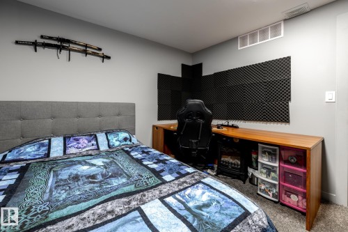 Bedroom featuring a tufted upholstered headboard, wall-mounted display rack, wood-finish desk, sound-dampening wall panels, and carpet flooring - 7 Doolan Place, St. Albert, AB - Indoor Photo Showing Bedroom