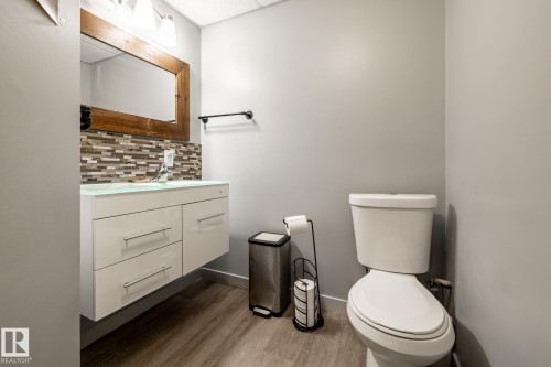 Floating vanity with an integrated basin, a mosaic tile backsplash, a wood-framed mirror, and wood-finish flooring - 7 Doolan Place, St. Albert, AB - Indoor Photo Showing Bathroom