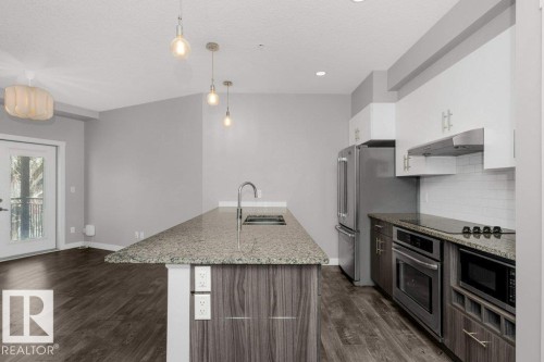 Modern kitchen featuring a granite-topped island with an integrated sink and gooseneck faucet - 204 10126 144 Street, Edmonton, AB - Indoor Photo Showing Kitchen With Stainless Steel Kitchen With Upgraded Kitchen
