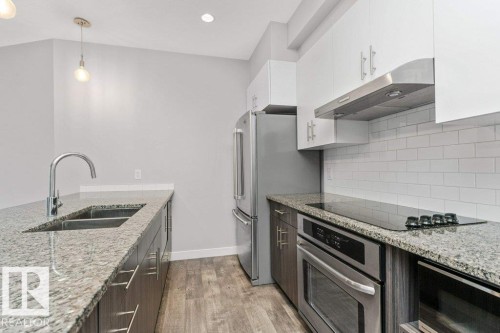 Contemporary kitchen featuring granite countertops, stainless steel appliances, a subway tile backsplash, white upper cabinetry, and wood-finish flooring - 204 10126 144 Street, Edmonton, AB - Indoor Photo Showing Kitchen With Stainless Steel Kitchen With Double Sink With Upgraded Kitchen