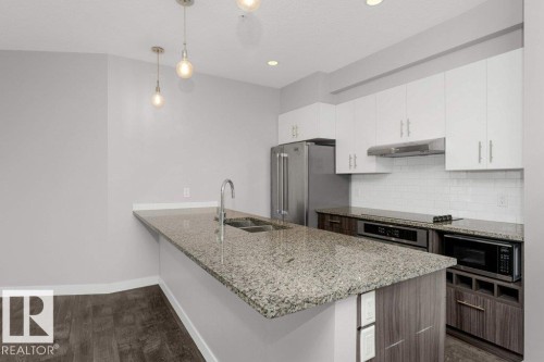 Kitchen featuring a large island with a double basin sink, stainless steel appliances, white upper cabinetry, and a white subway tile backsplash - 204 10126 144 Street, Edmonton, AB - Indoor Photo Showing Kitchen With Stainless Steel Kitchen With Double Sink With Upgraded Kitchen