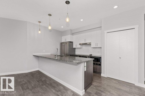 Kitchen featuring a granite-topped island with an undermount sink, stainless steel appliances, white flat-panel cabinetry, and wood-finish flooring - 204 10126 144 Street, Edmonton, AB - Indoor Photo Showing Kitchen With Upgraded Kitchen