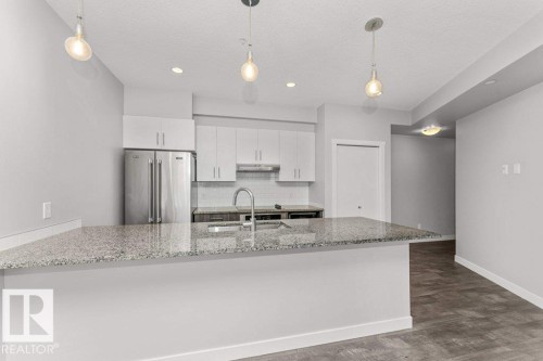 Kitchen featuring a large island with stone-finish countertop, stainless steel appliances, white cabinetry, and recessed lighting - 204 10126 144 Street, Edmonton, AB - Indoor Photo Showing Kitchen With Upgraded Kitchen