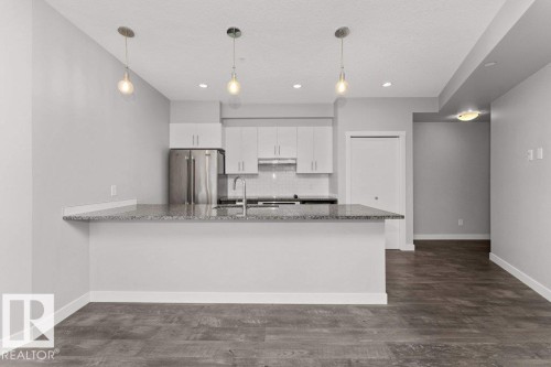 Kitchen featuring granite countertops, stainless steel appliances, white cabinetry, a subway tile backsplash, and three pendant lights over the breakfast bar - 204 10126 144 Street, Edmonton, AB - Indoor Photo Showing Kitchen With Upgraded Kitchen
