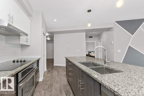 Modern kitchen featuring granite countertops, stainless steel appliances, white subway tile backsplash, a double basin sink, and wood-finish flooring - 204 10126 144 Street, Edmonton, AB - Indoor Photo Showing Kitchen With Double Sink With Upgraded Kitchen