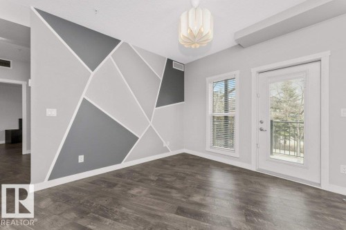 Interior space featuring wood-finish flooring, a geometric accent wall, and a contemporary ceiling fixture - 204 10126 144 Street, Edmonton, AB - Indoor Photo Showing Other Room