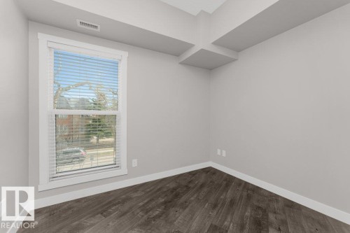Interior room featuring wood-finish flooring, light grey walls, white trim, and a window with blinds - 204 10126 144 Street, Edmonton, AB - Indoor Photo Showing Other Room