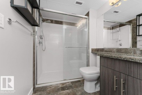 Bathroom featuring a glass-enclosed double shower, a modern toilet, a vanity with a stone countertop, wood-finish cabinetry, and tiled flooring - 204 10126 144 Street, Edmonton, AB - Indoor Photo Showing Bathroom