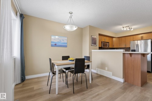 Open-concept dining area featuring wood-finish flooring, a contemporary pendant light fixture, and a window with sheer and blackout drapery - 17 171 Brintnell Boulevard, Edmonton, AB - Indoor Photo Showing Dining Room