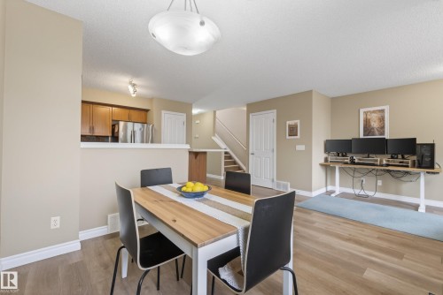 Open-concept living space featuring wood-finish flooring, a contemporary ceiling light fixture, a half-wall separating kitchen and dining areas, and a visible staircase - 17 171 Brintnell Boulevard, Edmonton, AB - Indoor Photo Showing Dining Room