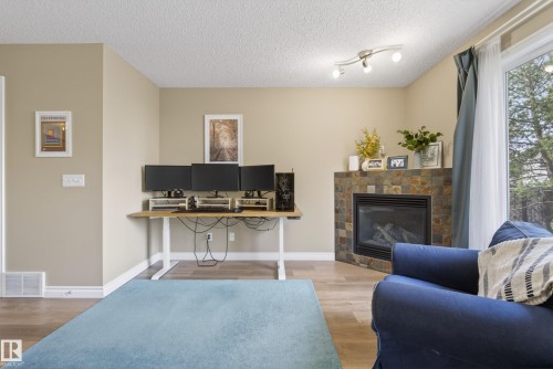 Living area featuring a corner fireplace with stone tile surround, wood-finish flooring, and a large sliding glass door - 17 171 Brintnell Boulevard, Edmonton, AB - Indoor Photo Showing Living Room With Fireplace