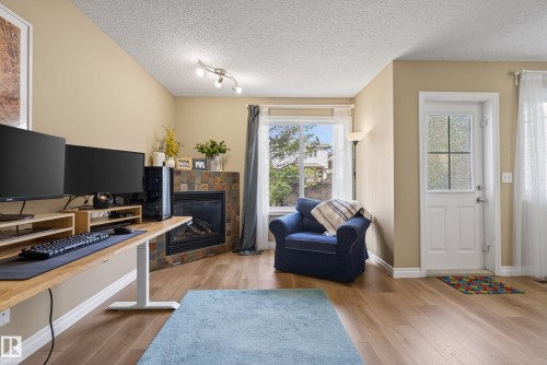 Open-concept living space featuring wood-finish flooring, a slate-tiled fireplace, and a white front entry door with privacy glass - 17 171 Brintnell Boulevard, Edmonton, AB - Indoor Photo Showing Living Room With Fireplace