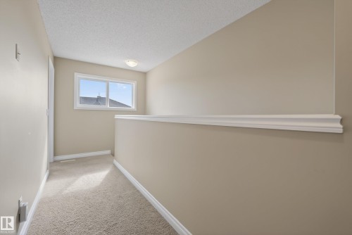 Upper-level hallway featuring a window with exterior residential roofline, neutral carpeting, and a decorative wall railing - 17 171 Brintnell Boulevard, Edmonton, AB - Indoor Photo Showing Other Room