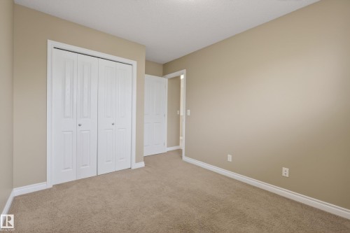 Neutral-toned room featuring a large bi-fold closet, textured carpet flooring, and white baseboards - 17 171 Brintnell Boulevard, Edmonton, AB - Indoor