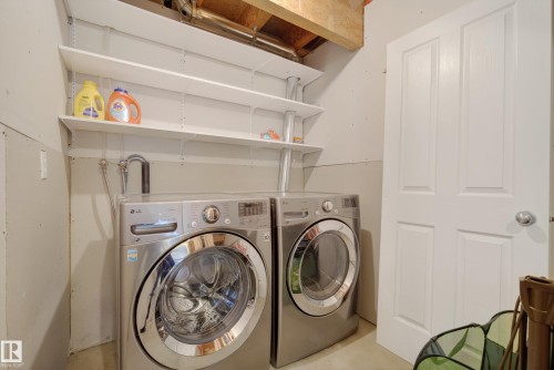 Dedicated laundry area featuring a front-load washer and dryer, adjustable wall-mounted shelving, exposed ceiling joists, and a four-panel interior door - 17 171 Brintnell Boulevard, Edmonton, AB - Indoor Photo Showing Laundry Room