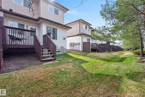 Rear exterior featuring a brown wood deck with stairs, beige siding, multiple windows, and a grassy lawn area - 17 171 Brintnell Boulevard, Edmonton, AB - Outdoor With Deck Patio Veranda