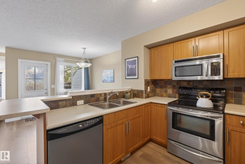 Kitchen featuring light wood-finish cabinetry, stainless steel appliances, a double basin sink, and a tiled backsplash - 17 171 Brintnell Boulevard, Edmonton, AB - Indoor Photo Showing Kitchen With Stainless Steel Kitchen With Double Sink