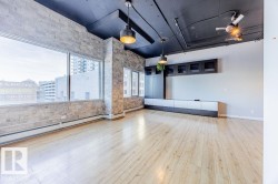 Expansive room featuring light wood-finish flooring, exposed brick walls, and large windows with urban scenery - 