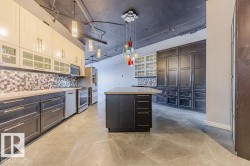 Spacious kitchen featuring an expansive island, two-tone cabinetry, stainless steel appliances, and a mosaic tile backsplash - 