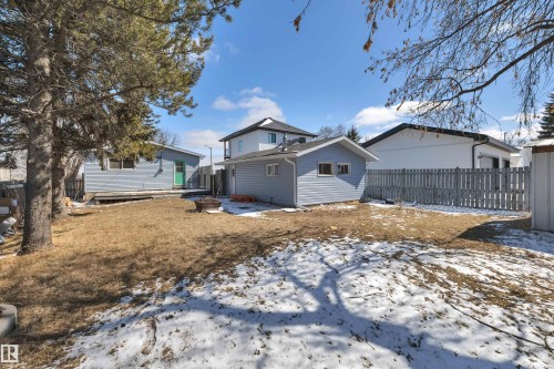 Expansive backyard featuring a detached accessory building, mature trees, partial fencing, and a separate structure with a green entry door - 4712 49 Street, Calmar, AB - Outdoor