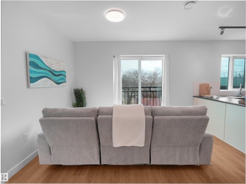 Open concept living area featuring wood-finish flooring, a contemporary ceiling light fixture, and a sliding glass door with a balcony access - 403 10115 88 Avenue, Edmonton, AB - Indoor Photo Showing Living Room