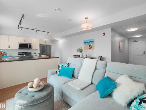 Open-concept living space featuring wood-finish flooring, a contemporary kitchen with stainless steel appliances, track lighting, and a white subway tile backsplash - 403 10115 88 Avenue, Edmonton, AB - Indoor
