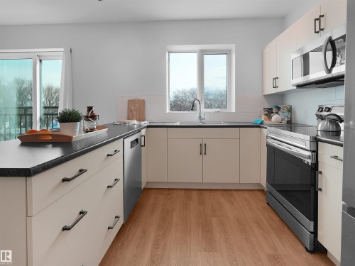 Kitchen featuring light wood-finish flooring, white cabinetry, dark countertops, and stainless steel appliances - 403 10115 88 Avenue, Edmonton, AB - Indoor Photo Showing Kitchen