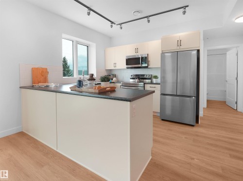 Modern kitchen featuring light-toned cabinetry, stainless steel appliances, a dark countertop, and wood-finish flooring - 403 10115 88 Avenue, Edmonton, AB - Indoor Photo Showing Kitchen