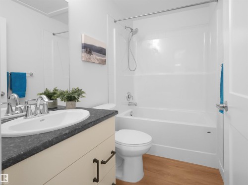 Bathroom featuring a white integrated tub and shower unit, a toilet, and a vanity with a dark countertop - 403 10115 88 Avenue, Edmonton, AB - Indoor Photo Showing Bathroom