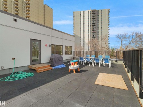 Expansive rooftop patio featuring dark tile flooring, metal railing, and a modern exterior building wall with multiple windows and a glass-paneled door - 403 10115 88 Avenue, Edmonton, AB - Outdoor