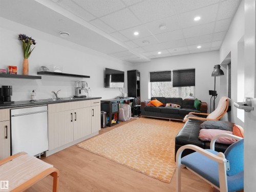 Spacious room featuring wood-finish flooring, a full wet bar with light wood cabinetry, integrated sink, and an under-counter refrigerator - 403 10115 88 Avenue, Edmonton, AB - Indoor