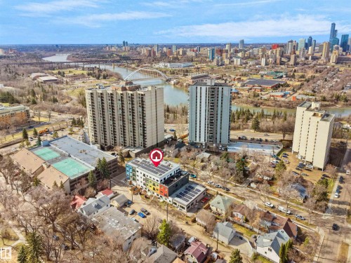 Modern building featuring a colorful facade, rooftop solar panels, surrounding urban landscape, and river with bridges - 403 10115 88 Avenue, Edmonton, AB - Outdoor With View