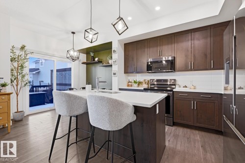The kitchen features dark wood cabinetry, stainless steel appliances, a white subway tile backsplash, and a large island with a light-colored countertop - 405 Genesis Court, Stony Plain, AB - Indoor Photo Showing Kitchen With Upgraded Kitchen
