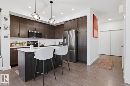 The kitchen features dark wood cabinetry, stainless steel appliances, and a central island with a white countertop - 405 Genesis Court, Stony Plain, AB - Indoor Photo Showing Kitchen