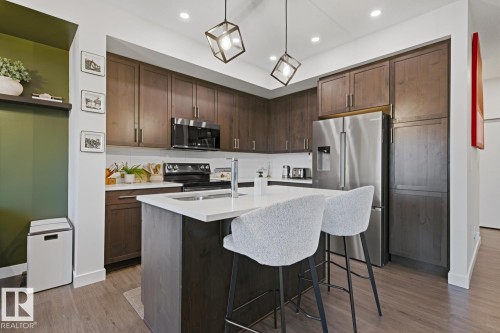 The kitchen features dark wood cabinetry, stainless steel appliances, and a central island with a white countertop and seating - 405 Genesis Court, Stony Plain, AB - Indoor Photo Showing Kitchen With Double Sink